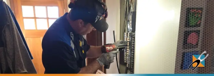 Electrician using a power drill to install wiring inside a residential electrical panel.