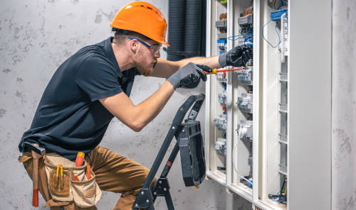 A male electrician works in a switchboard with an electrical connecting cable.